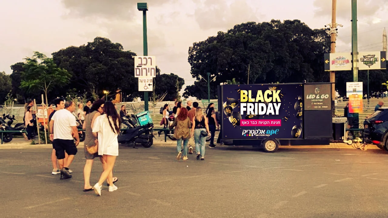 עוברי אורח ליד מסך נייד המציג מבצע BLACK FRIDAY של שקם אלקטריק
