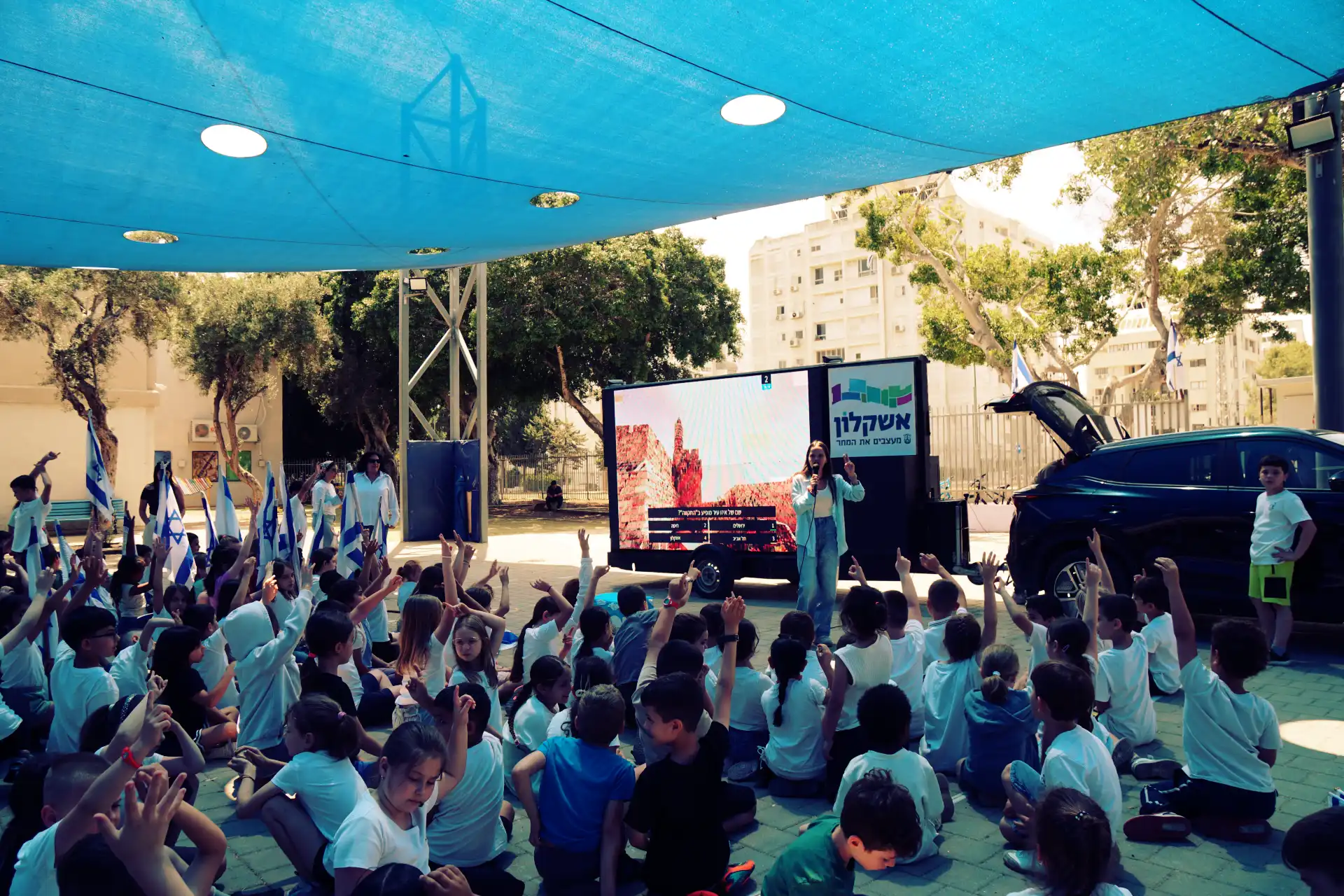 תלמידים יושבים מול מנחה ומסך LED בפעילות חוץ