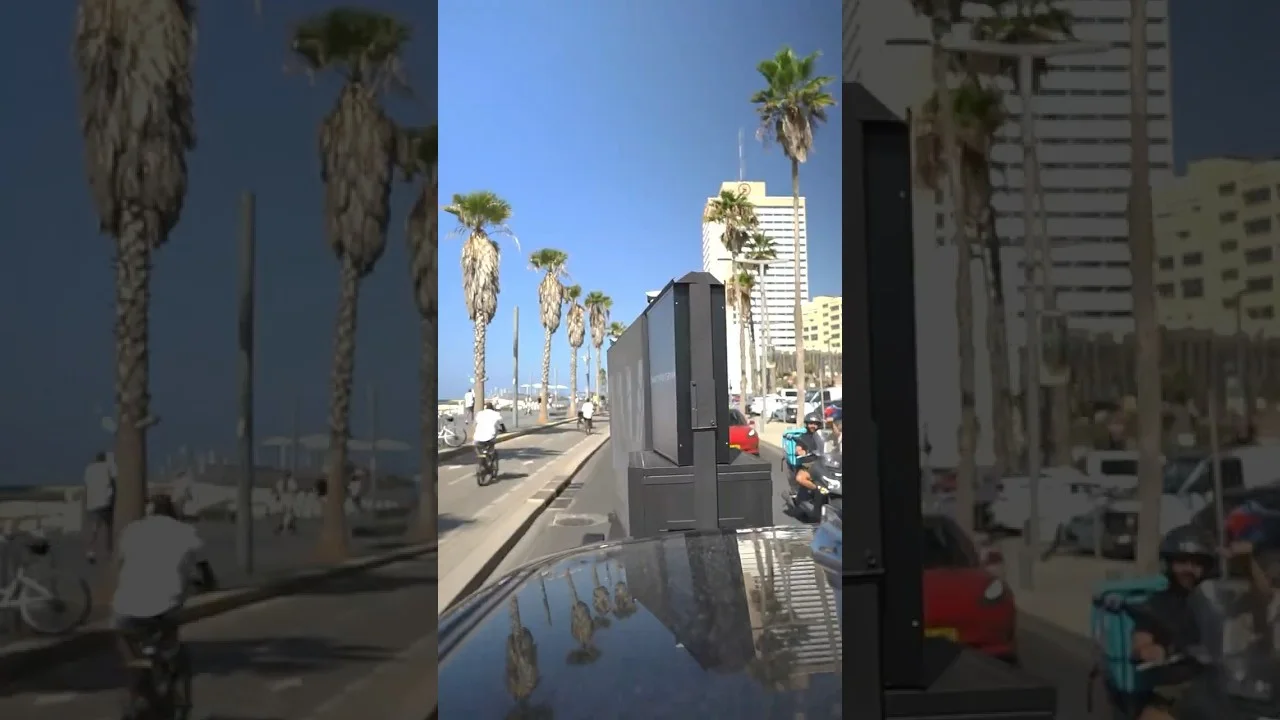 יחידת מסך ניידת נוסעת ברחוב עירוני שלאורכו עצי דקל