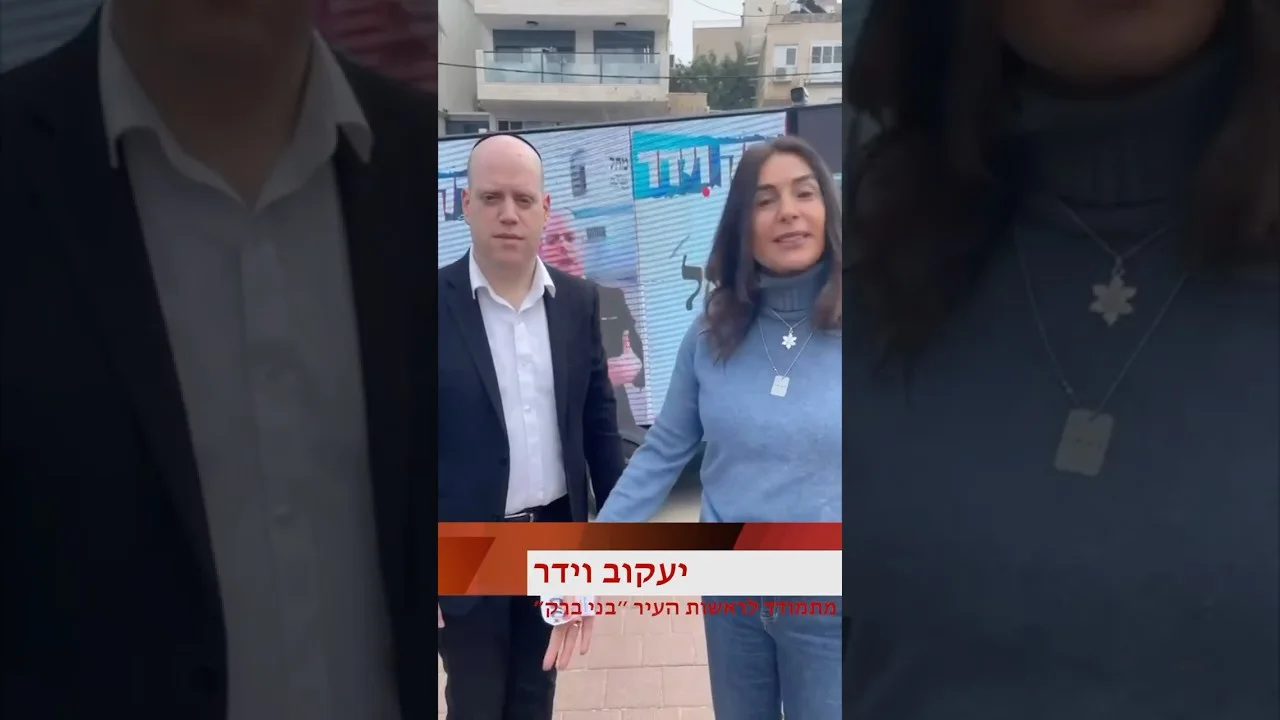 שני משתתפים עומדים מול מסך LED המציג מסר בחירות בבני ברק